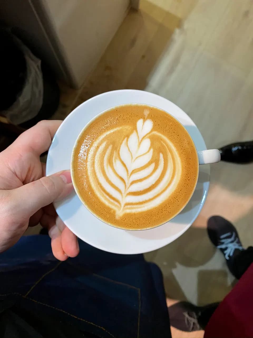 Cappuccino mit gegossener Rosette, von oben in der Hand gehalten